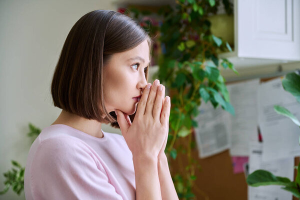 Profile view close-up of young womans face with hands folded in prayer, dreams, memories. Lifestyle, feelings, mental physical health, loneliness, stress, depression, difficulties, youth concept