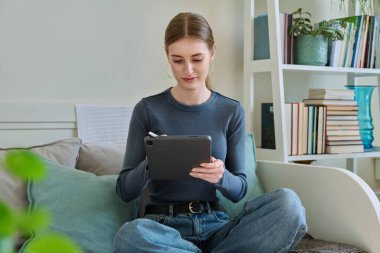 Dijital tabletli genç bir bayan. Stylus evde kanepede otururken resim çiziyor. Teknolojiler, eğlence, yaratıcılık, eğitim, serbest çalışma, yaşam tarzı, gençlik kavramı