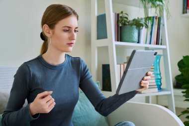 Genç kız öğrenci evde oturmuş dijital tabletin web kamerasıyla konuşuyor. 16,17,18 yaşında kız uzaktan eğitim, video konferans çağrısı, e-öğrenim teknolojisi eğitimi