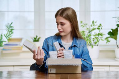 Tatmin olmuş genç bayan müşteri evde oturmuş online alımlarla dolu karton kutuları açıyor. Kozmetik ürünleri parfümleriyle dolu kutuları açan genç bir kız. Postayla teslimat, çevrimiçi mağaza