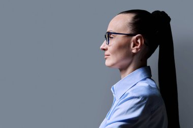 Orta yaşlı, ileriye bakan ciddi bir kadının profil görüntüsü, gri stüdyo arka planı, reklam metni için kopya alanı. 30 'lu yaşlarda kendine güvenen başarılı bir kadın. Pazarlama satış hizmetleri, insanlar