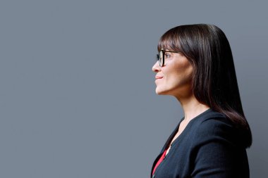 İleri bakan orta yaşlı bir kadının profil görüntüsü, gri stüdyo arka planı, reklam metni için kopya alanı. Olgun iş, kendine güvenen başarılı kadın. Pazarlama satış hizmetleri, insanlar