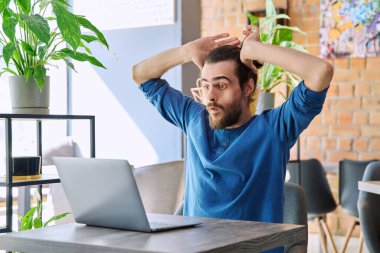 Kafedeki masada otururken dizüstü bilgisayara bakan heyecanlı, neşeli genç adam. Mutlu online haberler zafer başarı, duygular sevinç şoku