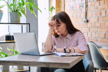 İş yerinde stresli baş ağrısı çeken endişeli, olgun bir kadın. Sağlık sorunları yaşlılık hormonal hastalıklar zihinsel zorluklar stresli iş, depresyon anksiyete ağrısı acı yaralanması