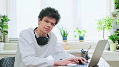 Masasında dizüstü bilgisayarı olan genç bir üniversite öğrencisi kameraya bakıyor. Evin içinde kulaklık takan yakışıklı, kıvırcık bir erkek. Eğitim, yaşam tarzı, gençlik 19,20 yaşında.