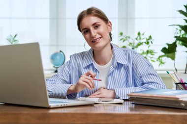 Lise öğrencisinin portresi, masada dizüstü bilgisayarla kameraya bakan gülümseyen genç bir bayan. Eğitim, eğitim, e-öğrenim, 16 bin 17 bin 18 yaşında gençlik