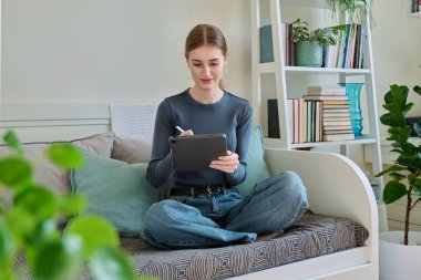 Dijital tabletli genç bir bayan. Stylus evde kanepede otururken resim çiziyor. Teknolojiler, eğlence, yaratıcılık, eğitim, serbest çalışma, yaşam tarzı, gençlik kavramı