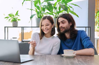 Mutlu gülümseyen genç çift kafeteryada otururken dizüstü bilgisayara bakıyorlar. İki kişilik boş zaman, yaşam tarzı, birliktelik, ilişki, iletişim, uzaktan çalışma