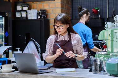 İş arkadaşları, kahve dükkanında tezgahın arkasında çalışan kadın ve erkek barista ve dizüstü bilgisayarla çalışan kadın. İş birliği personeli ortaklığı takım çalışması iş yönetimi küçük işletme