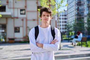 Portrait of confident smiling college student guy, young male with crossed arms with backpack looking at camera outdoor near educational building. Education, training, 19,20 years age youth concept clipart