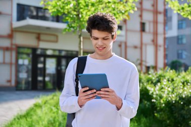 Genç yakışıklı üniversite öğrencisi dışarıda dijital tablet kullanıyor, eğitim binası geçmişi var. Eğitim, teknoloji, eğitim, 19-20 yaş gençlik kavramı