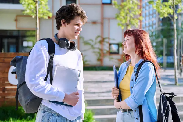 stock image Teenage college students guy and girl talking, standing outdoor near educational building. Youth 19-20 years old, education, lifestyle, friendship concept