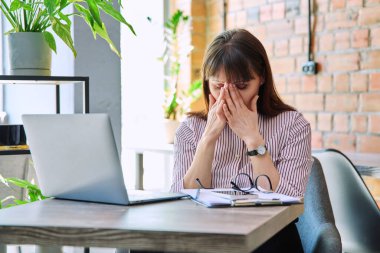 İş yerinde stresli baş ağrısı çeken endişeli, olgun bir kadın. Sağlık sorunları yaşlılık hormonal hastalıklar zihinsel zorluklar stresli iş, depresyon anksiyete ağrısı acı yaralanması