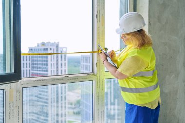 Kadın pencere tasarımcısı pencereyi mezurayla ölçüyor, perdeleri dikmek için ölçümler yazıyor yeni apartman dairesinde panjur yapıyor. Dekorasyon tasarım servisi