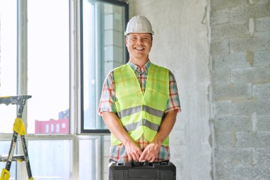 İnşaat alanında kasklı yelek ve alet çantasıyla çalışan sanayi işçisi erkek mühendisinin portresi. İnşaat onarım servisi geliştirme çalışma konsepti
