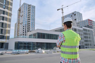 Kendine güvenen genç mühendis müteahhit endüstri işçisi inşaat sahasının arka tarafına bakıyor. Endüstri, teknik denetim, mühendislik hizmeti, geliştirme, iş kavramı