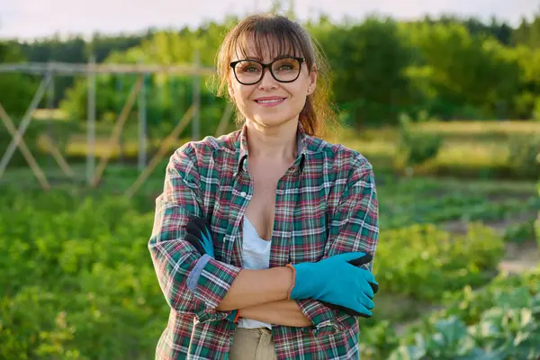 stock image Portrait of middle aged confident smiling woman in vegetable garden, outdoors, spring summer season. Female farmer, gardener with crossed arms looking at camera. Agriculture horticulture cultivation