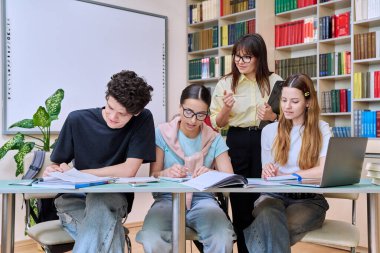 Bayan akıl hocası ile aynı masada oturan bir grup genç öğrenci kütüphane ofisinde yapılacak sınavlara hazırlanıyor. Lise, eğitim, takım çalışması, öğrenme, ergenlik kavramı