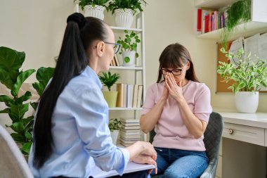 Psikologla terapi seansında terapi gören olgun üzgün bir kadın terapist sosyal hizmet görevlisinin ofisinde masada oturuyor. Psikoloji psikoterapi zihinsel tedavi desteği