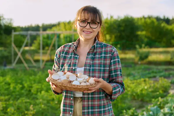 stock image Middle aged woman with eggshell in wicker bowl, outdoor, garden background. Natural organic bio fertilizers for growing herbs vegetables berries