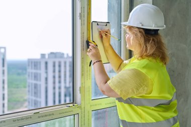 Kadın pencere tasarımcısı pencereyi mezurayla ölçüyor, perdeleri dikmek için ölçümler yazıyor yeni apartman dairesinde panjur yapıyor. Dekorasyon tasarım servisi