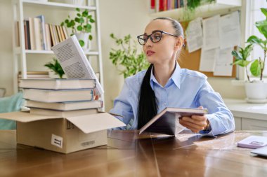 İnternetteki bir dükkandan gelen karton kutulardan yeni kitap almış bir kadın. Çevrimiçi alışveriş, paketleri açma, kurgu kitapları okuma, kurgusal olmayan edebiyat, hobi ve eğlence kavramı