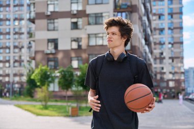 Sırt çantalı, basketbol topu dışarıda yürüyen, modern şehir geçmişi olan yakışıklı üniversite öğrencisi. Gençlik, aktif yaşam tarzı, şehir tarzı konsepti