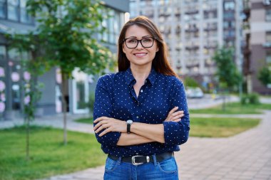 Kollarını kavuşturmuş kenar mahalle tarzında poz veren olgun, kendine güvenen bir kadının portresi. Yaşam tarzı, orta yaş, iş hayatı, başarı mutluluk kavramı