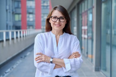 Kollarını kavuşturmuş kenar mahalle tarzında poz veren olgun, kendine güvenen bir kadının portresi. Yaşam tarzı, orta yaş, iş hayatı, başarı mutluluk kavramı