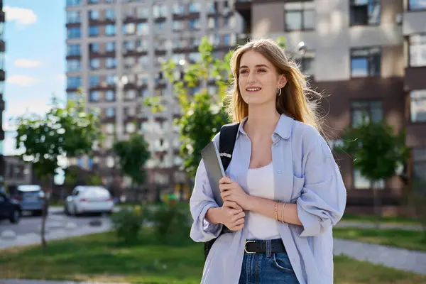 stock image Walking young smiling female college student with backpack holding laptop computer outdoor, modern urban background, copy space. Education, technology, training, 17, 18 years age youth concept