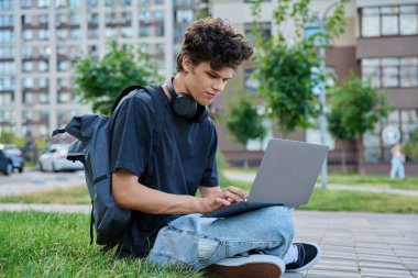Şehirde dizüstü bilgisayar kullanan genç bir erkek. Yakışıklı bir öğrenci, 19-20 yaşlarında, boş zamanlarında bilgisayar kullanıyor, okuyor, çalışıyor. Teknoloji, gençlik, eğitim, kentsel tarz kavramı