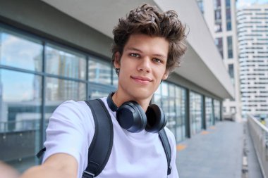 Selfie portrait of young happy handsome man with curly hair, guy university college student outdoor. Youth, urban style, 19,20 years male, lifestyle concept clipart