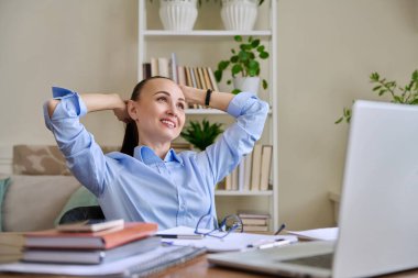 İş yerinde elleri başının arkasında dizüstü bilgisayarla duran sakin ve rahat bir iş kadını. Tatmin olmuş bir kadın mola veriyor, zihin huzuru, stres eksikliği