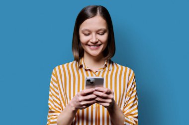 Genç iş kadını mavi arka planda akıllı telefon kullanıyor. Gülümseyen çekici bir bayanın mesajlaşması. Teknoloji mobil uygulamaları İnternet iş dünyası iletişim eğitimi