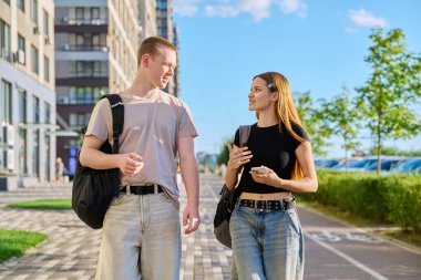 Yürüyen arkadaşlar, kız ve erkek, kolej öğrencileri modern şehrin caddelerinde birlikte yürüyorlar. Gençlik 18-20 yaş arası, arkadaşlık, iletişim, kentsel yaşam tarzı kavramı