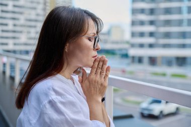 Dua ederken el ele tutuşan olgun, ciddi bir kadın. Yüzü kapalı, şehir dışı geçmişi var. Din, umut, yaşam tarzı, olgunluk, zihinsel yaşam, insan kavramı