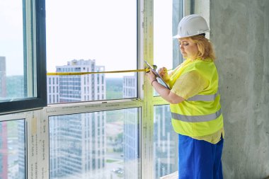 Kadın pencere tasarımcısı pencereyi mezurayla ölçüyor, perdeleri dikmek için ölçümler yazıyor yeni apartman dairesinde panjur yapıyor. Dekorasyon tasarım servisi