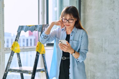 Kadın dekoratör, tamirci, yeni apartman ofisindeki akıllı telefonu kullanarak son bitirme ve dekorasyon organizatörü. Onarım, dekorasyon, iş, insan kavramı