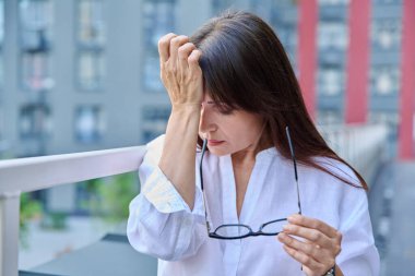 Stres, baş ağrısı, menopoz semptomları, sağlık sorunları, açık hava modern şehir geçmişi olan olgun bir kadın. Depresyon, stres, zorluklar, zihinsel sağlık konsepti
