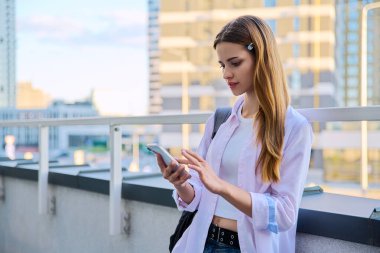 Akıllı telefon kullanan genç bir kadın, modern şehir geçmişi. Ergen öğrenci gezmek için mobil uygulama uygulamaları kullanarak mesajlaşıyor. Teknoloji İnternet Eğitim Gençlik Usulü