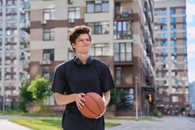 Sırt çantalı, basketbol topu dışarıda yürüyen, modern şehir geçmişi olan yakışıklı üniversite öğrencisi. Gençlik, aktif yaşam tarzı, şehir tarzı konsepti