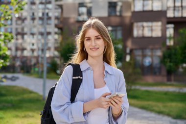 Akıllı telefon kullanan, modern şehir geçmişi olan genç sarışın bir kadın. Ergen öğrenci gezmek için mobil uygulama uygulamaları kullanarak mesajlaşıyor. Teknoloji İnternet Eğitim Gençlik Usulü