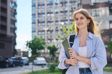 Sırt çantasıyla gezen genç, gülümseyen bir üniversite öğrencisi kucağında dizüstü bilgisayar, modern şehir geçmişi, fotokopi alanı. Eğitim, teknoloji, eğitim, 17-18 yaş gençlik kavramı