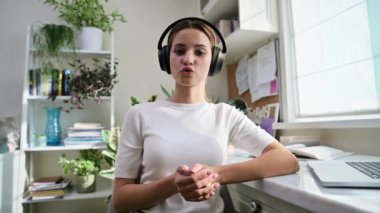 Webcam 'de, kulaklık takan, web kamerasında konuşan, masasında oturan genç kız öğrenci portresi. İnternet çevrimiçi webinar, görüntülü sohbet çağrı konferansı, teknoloji eğitimi