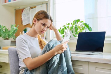 Evde akıllı telefonuyla oturan üzgün, yalnız genç bir kadın. 17-19 yaşlarında hayal kırıklığına uğramış bir kız, üzgün bir üniversite öğrencisi. Depresyon, stres, zihinsel zorluklar, gençlik kavramı