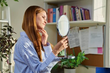 Genç ve güzel bir kadın aynada cilt makyajına bakıyor. Güzellik ve sağlık ürünleri