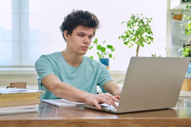 Masasında oturan genç bir üniversite öğrencisi, dizüstü bilgisayarda yazıyor. 19-20 yaşlarında evde eğitim amaçlı bilgisayar kullanan bir çocuk. Teknoloji eğitimi gençlik kavramı