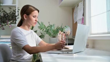 Genç kız üniversite öğrencisi video konferans sohbeti yapıyor toplantı dersi webinar bilgisayar ekranında, evde masa başında oturuyor. E-öğrenme, eğitim, teknoloji, bilgi, gençlik