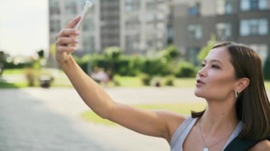 Genç ve güzel bir kadın akıllı telefondan görüntülü konuşma yapıyor. Şehir dışında. Çevrimiçi toplantı, video iletişimi, teknoloji, yaşam tarzı, gençlik kavramı