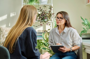 Dijital tabletli bayan psikolog ofiste genç bir kadınla terapi seansı yapıyor. Gençliğin akıl sağlığı, profesyonel psikolojik destek danışmanlık, psikoterapi hizmetleri